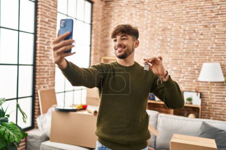 Téléchargez les photos : Jeune homme arabe faire selfie par smartphone tenant la clé à la nouvelle maison - en image libre de droit