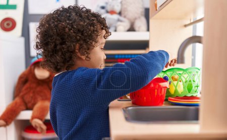 Foto de Adorable hispanic boy playing with play kitchen standing at kindergarten - Imagen libre de derechos