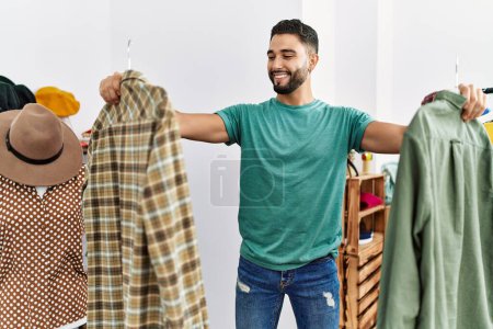 Téléchargez les photos : Jeune homme arabe client souriant achats confiants au magasin de vêtements - en image libre de droit