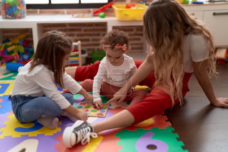 Foto de Profesor con las niñas jugando con las matemáticas juego de puzzle sentado en el suelo en el jardín de infantes - Imagen libre de derechos