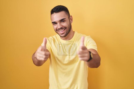 Téléchargez les photos : Jeune homme hispanique debout sur fond jaune pointant les doigts vers la caméra avec un visage heureux et drôle. bonne énergie et vibes. - en image libre de droit