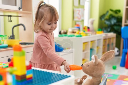 Photo for Adorable blonde girl play feeding rabbit doll at kindergarten - Royalty Free Image