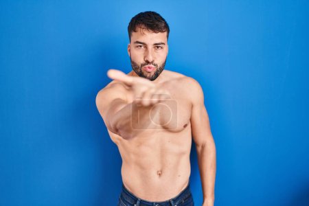 Foto de Handsome hispanic man standing shirtless looking at the camera blowing a kiss with hand on air being lovely and sexy. love expression. - Imagen libre de derechos
