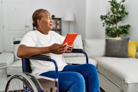 Foto de Senior african american woman using touchpad sitting on wheelchair at home - Imagen libre de derechos