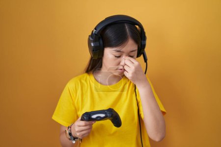 Foto de Chinese young woman playing video game holding controller tired rubbing nose and eyes feeling fatigue and headache. stress and frustration concept. - Imagen libre de derechos
