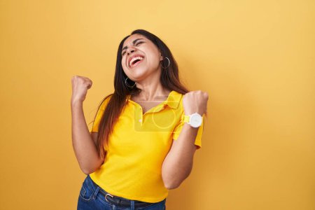Téléchargez les photos : Jeune femme arabe debout sur fond jaune célébrant surpris et étonnés pour le succès avec les bras levés et les yeux fermés. concept gagnant. - en image libre de droit