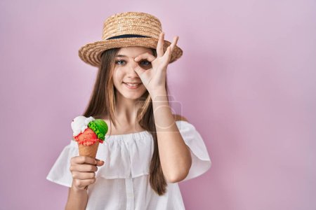 Photo for Teenager girl holding ice cream doing ok gesture with hand smiling, eye looking through fingers with happy face. - Royalty Free Image