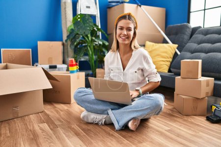 Photo for Young hispanic woman using laptop sitting on floor at new home - Royalty Free Image
