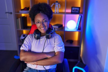 Photo for African american woman streamer smiling confident sitting with arms crossed gesture at gaming room - Royalty Free Image