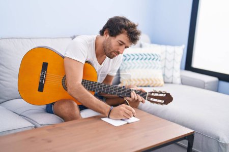 Photo for Young hispanic man playing classical guitar composing song at home - Royalty Free Image