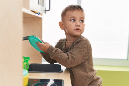 Photo for Adorable hispanic boy playing with play kitchen standing at kindergarten - Royalty Free Image