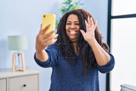 Foto de Mujer hispana de tamaño grande haciendo videollamadas con smartphone con aspecto positivo y feliz de pie y sonriendo con una sonrisa confiada mostrando los dientes - Imagen libre de derechos