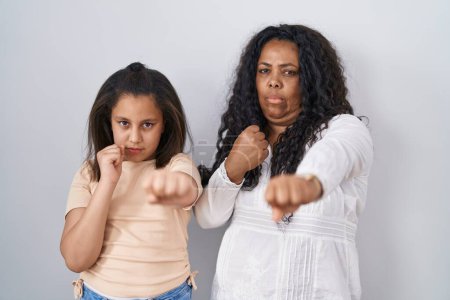 Téléchargez les photos : Mère et jeune fille debout sur fond blanc frappant poing pour se battre, attaque agressive et en colère, menace et violence - en image libre de droit