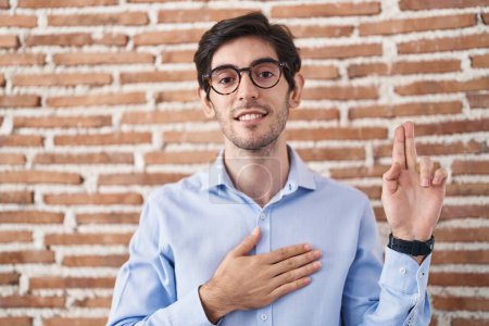 Téléchargez les photos : Young hispanic man standing over brick wall background smiling swearing with hand on chest and fingers up, making a loyalty promise oath - en image libre de droit