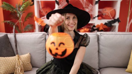 Foto de Joven rubia teniendo fiesta de halloween sosteniendo cesta de calabaza en casa - Imagen libre de derechos