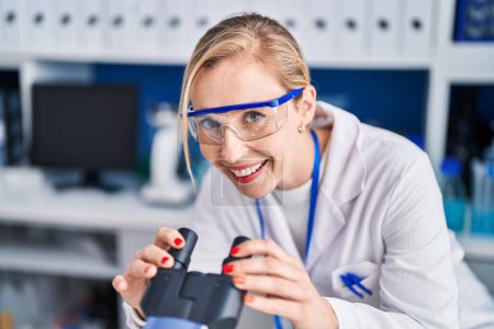 Photo for Young blonde woman scientist smiling confident using microscope at laboratory - Royalty Free Image