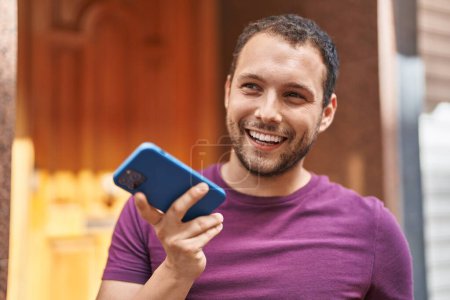 Téléchargez les photos : Jeune homme souriant confiant parler sur le smartphone à la rue - en image libre de droit