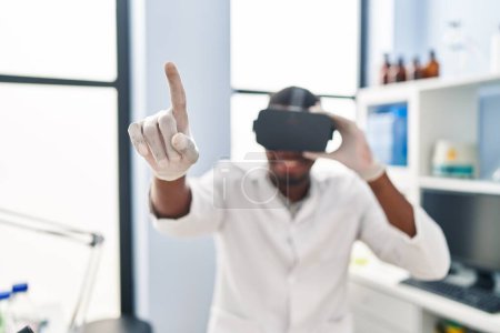 Téléchargez les photos : Jeune homme afro-américain portant l'uniforme de scientifique à l'aide de lunettes de réalité virtuelle au laboratoire - en image libre de droit
