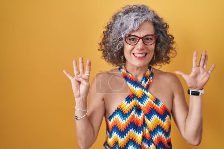 Foto de Mujer de mediana edad con el pelo gris de pie sobre el fondo amarillo que muestra y señala hacia arriba con los dedos número nueve mientras sonríe confiado y feliz. - Imagen libre de derechos