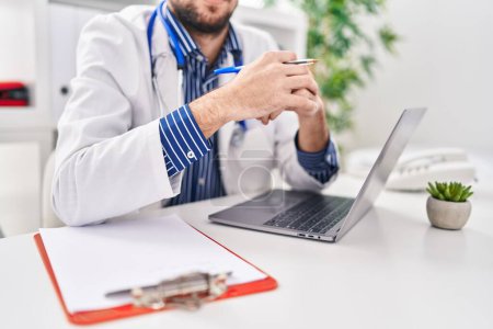 Photo for Young man doctor using laptop speaking at clinic - Royalty Free Image