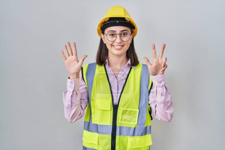 Foto de Chica hispana vistiendo uniforme constructor y hardhat mostrando y señalando hacia arriba con los dedos número ocho mientras sonríe confiado y feliz. - Imagen libre de derechos
