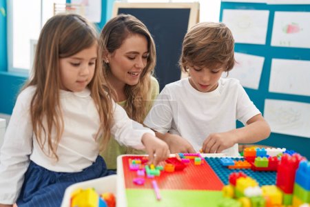 Foto de Profesor con niño y niña jugando con bloques de construcción sentados en la mesa en el jardín de infantes - Imagen libre de derechos