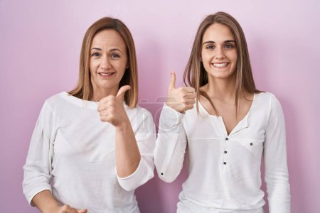Photo for Middle age mother and young daughter standing over pink background doing happy thumbs up gesture with hand. approving expression looking at the camera showing success. - Royalty Free Image