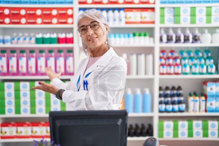 Foto de Mujer de mediana edad con tatuajes trabajando en farmacia invitando a entrar sonriendo natural con la mano abierta - Imagen libre de derechos