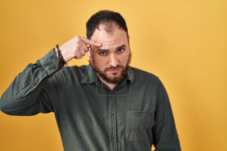 Photo for Plus size hispanic man with beard standing over yellow background pointing unhappy to pimple on forehead, ugly infection of blackhead. acne and skin problem - Royalty Free Image
