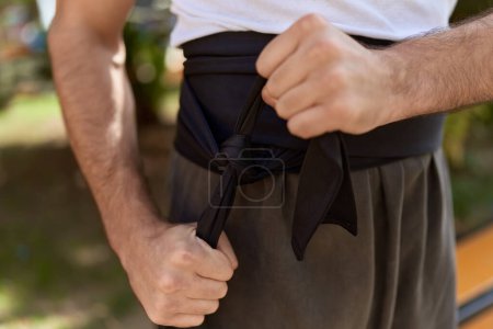 Photo for Young hispanic man karate fighter tying belt at park - Royalty Free Image