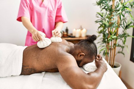 Téléchargez les photos : Young african american man having back massage with thai bags at beauty center - en image libre de droit