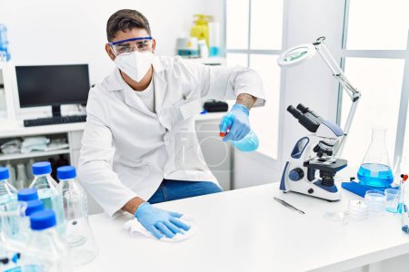 Téléchargez les photos : Bel homme hispanique travaillant comme scientifique nettoyer la table au laboratoire - en image libre de droit