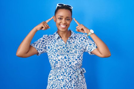 Photo for African american woman standing over blue background smiling pointing to head with both hands finger, great idea or thought, good memory - Royalty Free Image