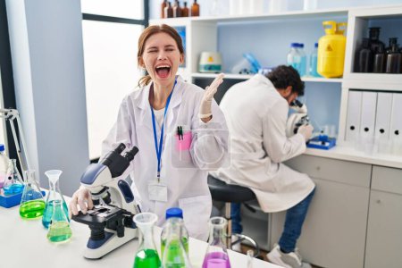 Photo for Young two people working at scientist laboratory celebrating victory with happy smile and winner expression with raised hands - Royalty Free Image