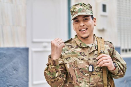 Téléchargez les photos : Jeune homme arabe portant un uniforme de camouflage de l'armée à l'extérieur pointant le pouce vers le côté souriant heureux avec la bouche ouverte - en image libre de droit