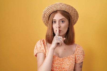 Téléchargez les photos : Young redhead woman standing over yellow background wearing summer hat asking to be quiet with finger on lips. silence and secret concept. - en image libre de droit