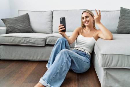 Foto de Mujer rubia joven sonriendo confiada haciendo selfie por el teléfono inteligente en casa - Imagen libre de derechos