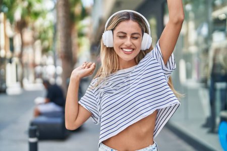 Téléchargez les photos : Young blonde woman listening to music and dancing at street - en image libre de droit