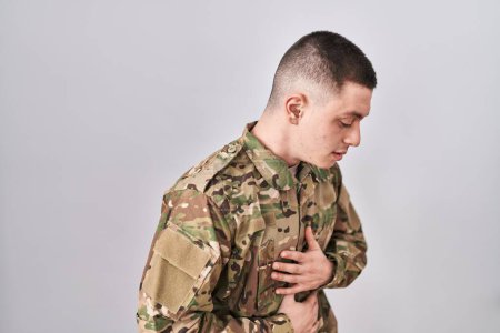 Téléchargez les photos : Jeune homme portant un uniforme de camouflage de l'armée avec la main sur le ventre parce que les nausées, la maladie douloureuse se sentent mal. concept de douleur. - en image libre de droit