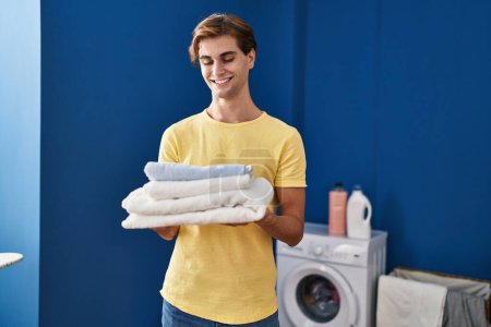 Foto de Young caucasian man smiling confident holding folded towels at laundry room - Imagen libre de derechos