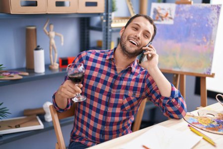 Photo for Young man artist talking on smartphone drinking wine at art studio - Royalty Free Image