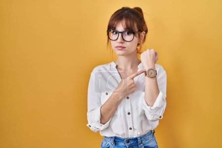 Photo for Young beautiful woman wearing casual shirt over yellow background in hurry pointing to watch time, impatience, looking at the camera with relaxed expression - Royalty Free Image