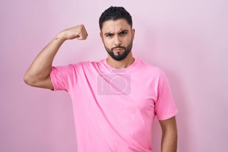 Photo for Hispanic young man standing over pink background strong person showing arm muscle, confident and proud of power - Royalty Free Image