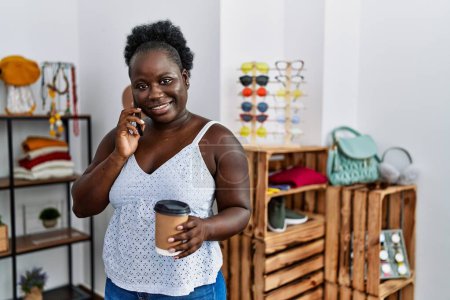 Photo for Young african american woman customer talking on the smartphone and drinking coffee at clothing store - Royalty Free Image