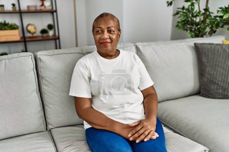 Foto de Senior africana americana mujer sonriendo confiado sentado en sofá en casa - Imagen libre de derechos