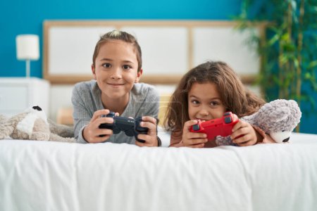 Foto de Two kids playing video game lying on bed at bedroom - Imagen libre de derechos