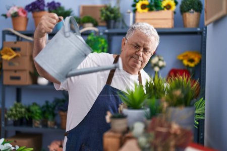 Photo for Middle age grey-haired man florist watering plant at florist - Royalty Free Image