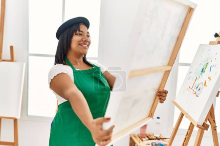 Photo for Hispanic brunette woman holding canvas proud of painting at art studio - Royalty Free Image