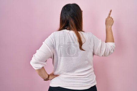 Photo for Pregnant woman standing over pink background posing backwards pointing ahead with finger hand - Royalty Free Image
