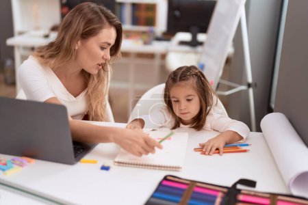 Photo for Teacher and toddler sitting on table drawing on notebook at classroom - Royalty Free Image